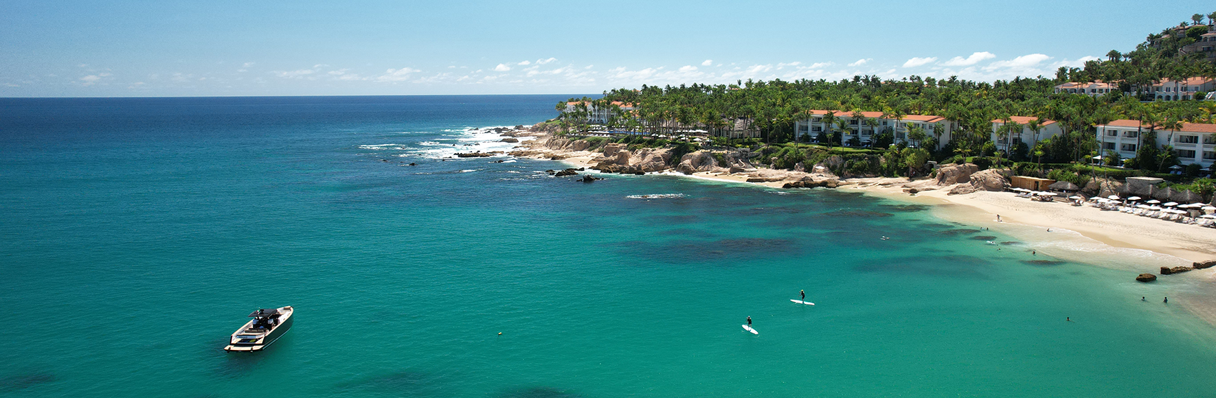 Aerial view of Playa Palmilla’s turquoise waters, sandy beach, rocky coastline, and palm-lined residences in Los Cabos.