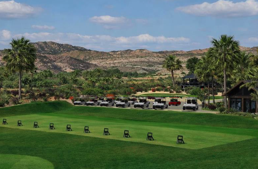 One&Only Palmilla Golf Club practice range with target greens, bunkers, palm trees, and views toward the Sea of Cortez.