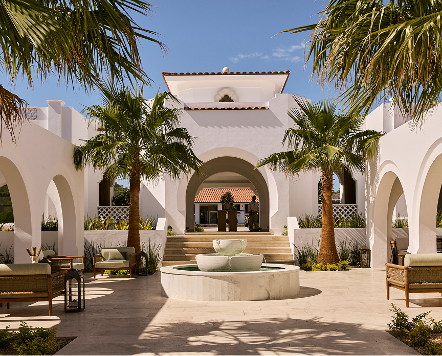 Elegant courtyard at One&Only Palmilla featuring white stucco arches, palm trees, and a central stone fountain, with lounge seating and a serene, sunlit atmosphere.