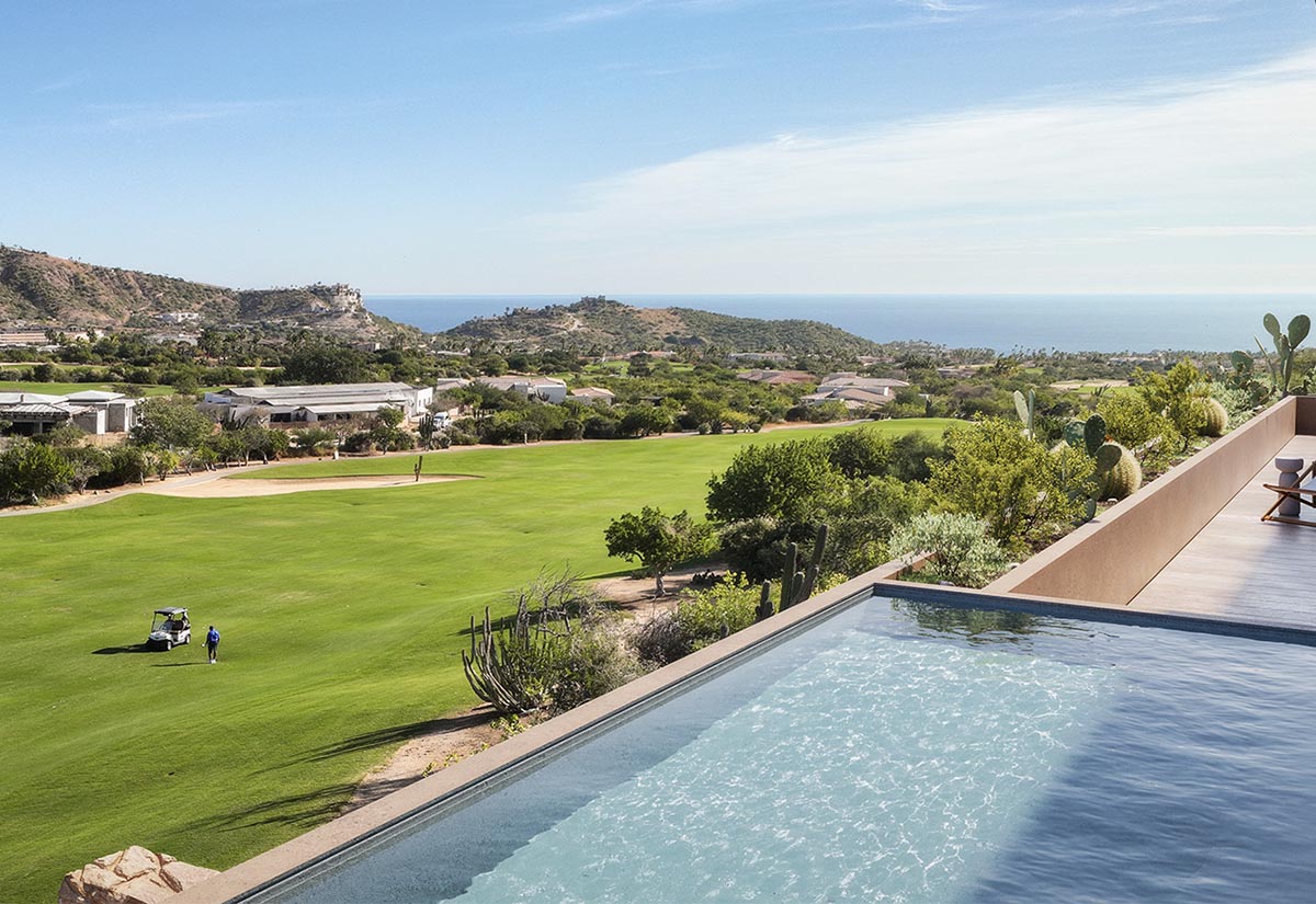 View from a Mountain Residences terrace overlooking a lush golf fairway, with an infinity-edge pool in the foreground, desert landscaping and cacti along the edge, and distant hills leading to the blue waters of the Sea of Cortez under a clear sky.