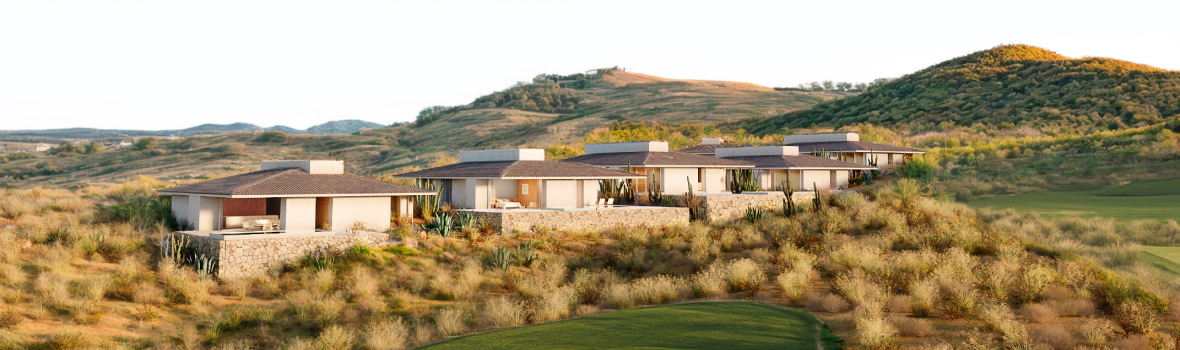Contemporary Valley Estate homes set along a desert hillside, featuring low-profile architecture with stone and stucco finishes, overlooking a lush golf fairway with rolling hills in the background.